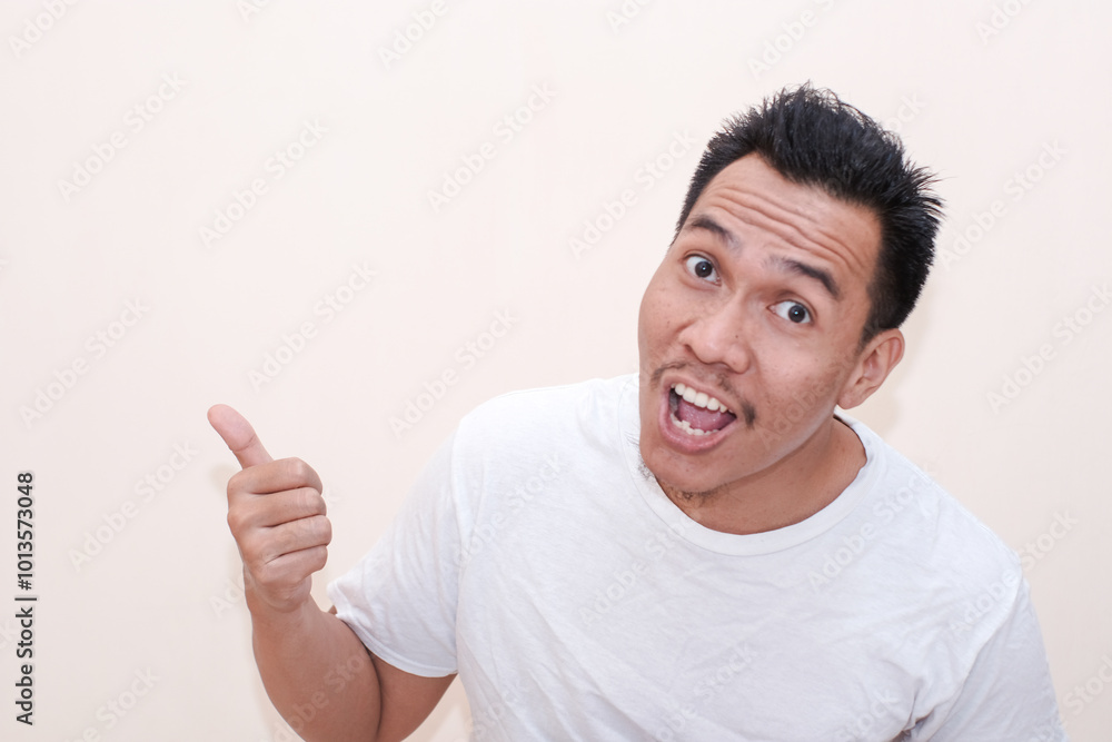 Smile and happy face of a Southeast Asian man wearing white t-shirt and point to present an empty space of content. Advertising model concept. Smile and happy face of a Southeast Asian man wearing white t-shirt and point to present an empty space of content. Advertising model concept.