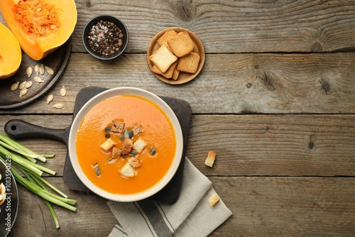 Delicious pumpkin soup in bowl and ingredients on wooden table, flat lay. Space for text