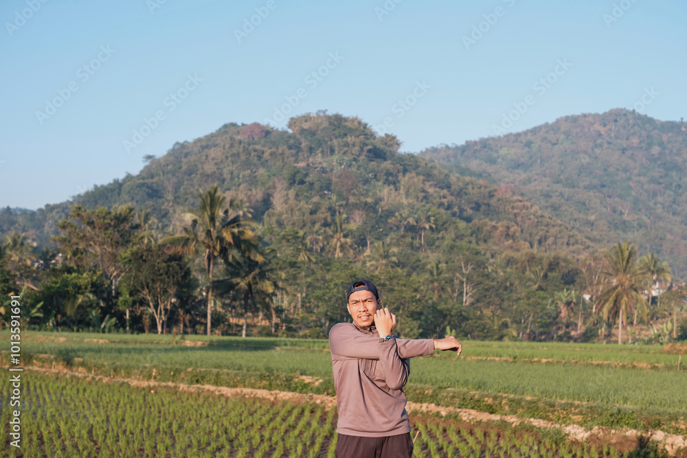 A Southeast Asian man wearing grey jacket with blue cap stretching arms for fitness, exercise and health, preparation and ready. Athlete, happy and warm up start outdoor for workout A Southeast Asian man wearing grey jacket with blue cap stretching arms for fitness, exercise and health, preparation and ready. Athlete, happy and warm up start outdoor for workout