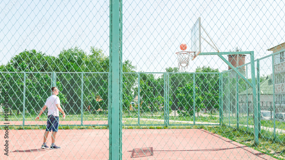 Active young male playing street basketball, dribbling ball, training on court Active young male playing street basketball, dribbling ball, training on court