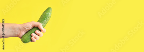 Fotografija Ripe cucumber in a woman's hand on a yellow background
