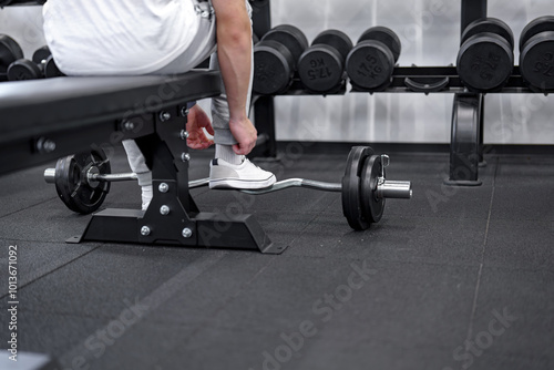 A man in a gym preparing to do an exercise with an EZ bar on a bench.