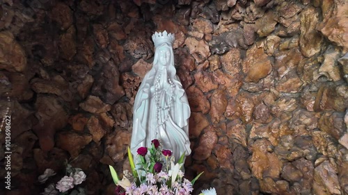 4k low angle video footage of A large white statue of Mary made of stone carvings in grottoes with flowers and candles lit decoration.