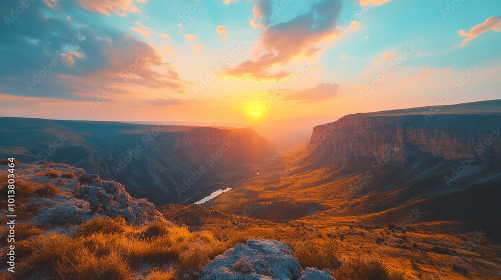 Fototapeta premium A stunning sunset over a vast canyon with a river winding through the valley, casting a warm glow over the landscape.