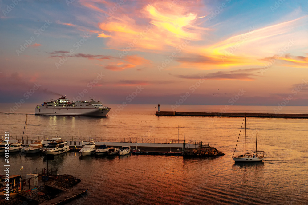 Fototapeta premium yacht enters marina as ferry enters commercial harbor next to lighthouse in beautiful sunset
