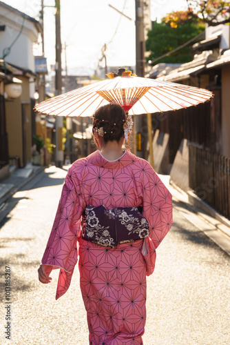 A woman in a pink kimono holds a Japanese traditional umbrella walking on the street. Kyoto, Japan.