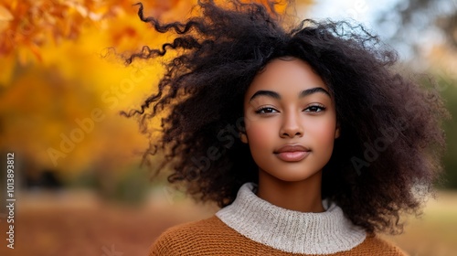 A portrait of a black woman walking through an open field of fall foliage, her hair flowing in the breeze.