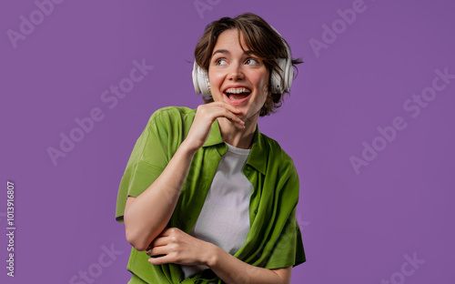 Happy woman gets high, listening music, enjoying dance with headphones on violet studio backdrop. Radio, wireless modern sound technology, online player photo