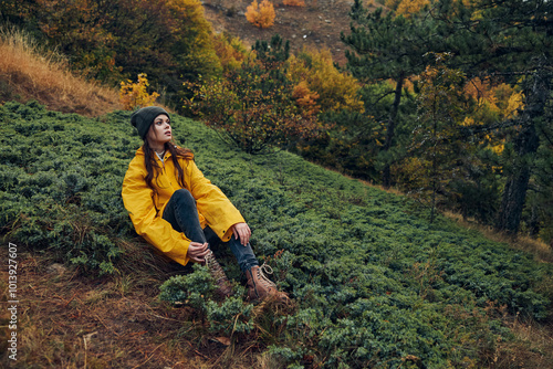 Φωτογραφία Beautiful young woman in yellow jacket sitting alone on grassy hill surrounded b