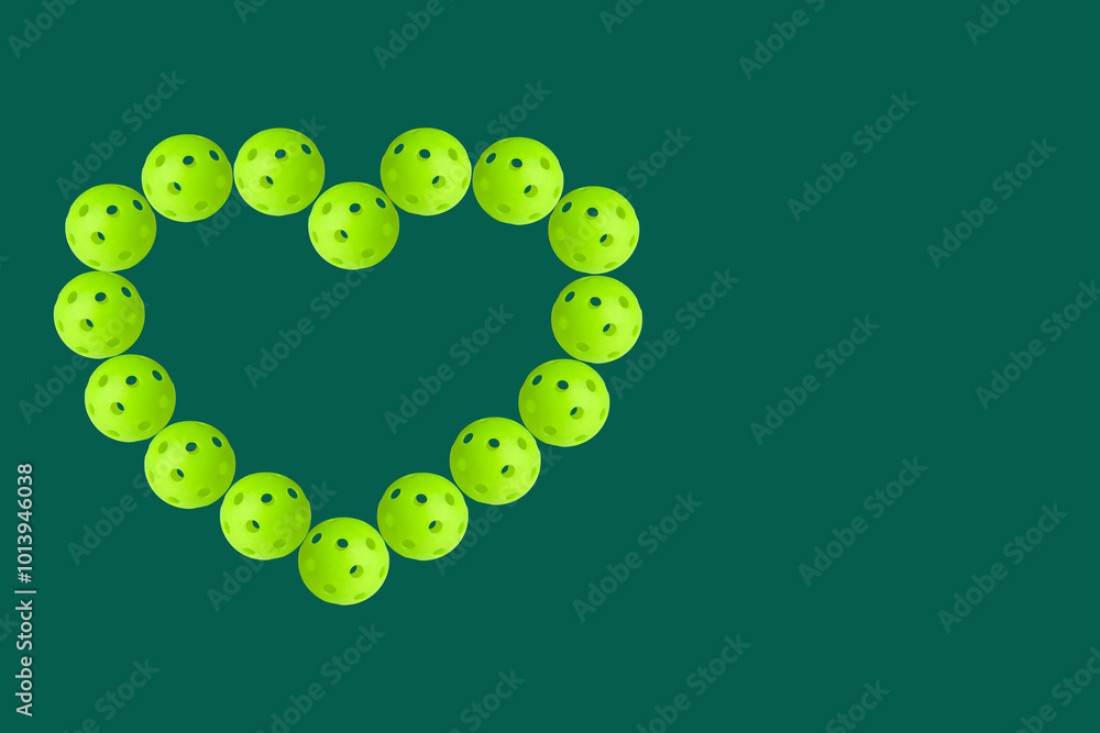 Heart shaped pattern made of green pickleballs on green background.