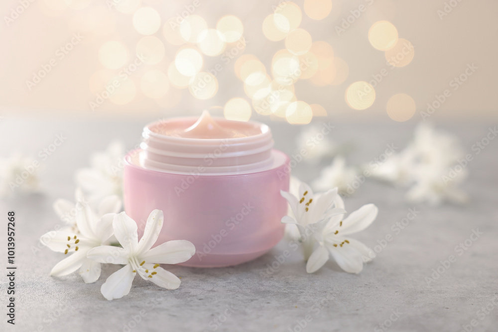 Cream in jar and jasmine flowers on grey table against light background with blurred lights, closeup Cream in jar and jasmine flowers on grey table against light background with blurred lights, closeup