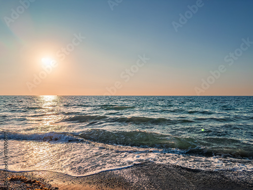 Sunset Over a Tranquil Sea With Gentle Waves Lapping on the Sandy Shore, Captured in Serene Light During Evening Hours