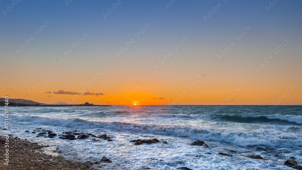 Naklejka premium Stunning Sunset Over the Ocean Waves With Rocky Shoreline During Evening on a Clear Day