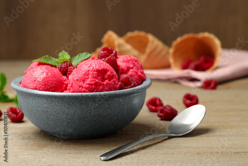 Delicious raspberry sorbet with fresh berries in bowl and spoon on wooden table