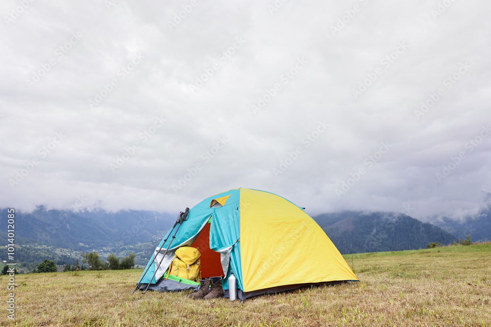 Camping tent and tourist stuff on grass in mountains