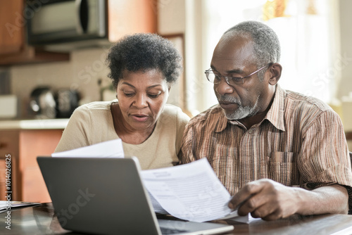 Senior couple reviewing financial documents together on a laptop, symbolizing retirement planning and budgeting. 