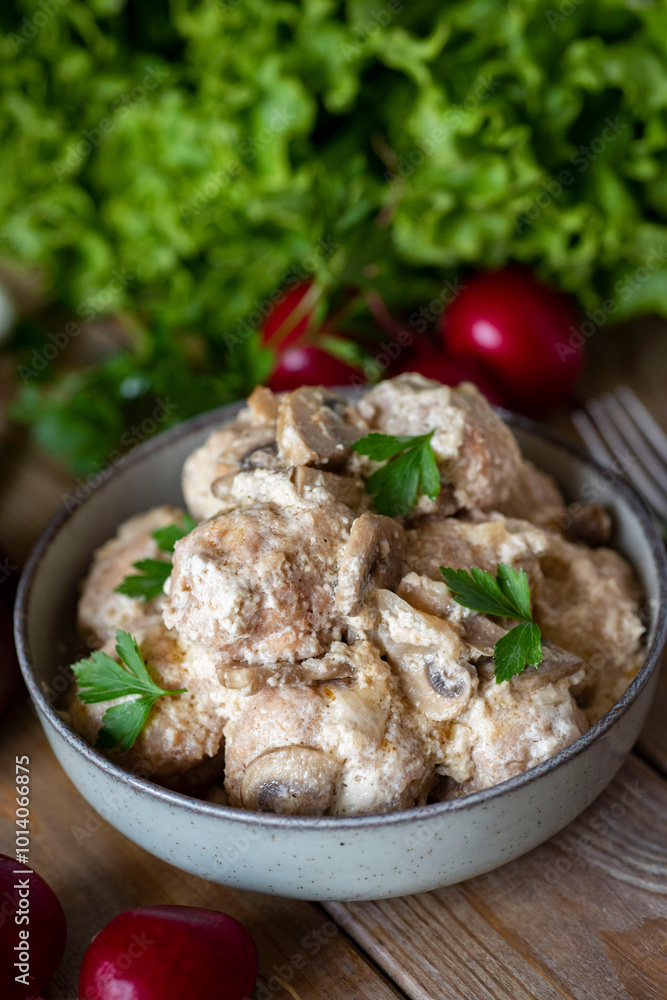 Meatballs in cream sauce with mushrooms in a plate on a gray background. A hearty lunch. Pork meatballs with mushrooms. Vertical photo. close-up Meatballs in cream sauce with mushrooms in a plate on a gray background. A hearty lunch. Pork meatballs with mushrooms. Vertical photo. close-up