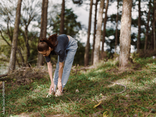 Young woman bending down to pick wildflowers in a serene forest, surrounded by tall trees and lush greenery, enjoying nature s beauty and tranquility