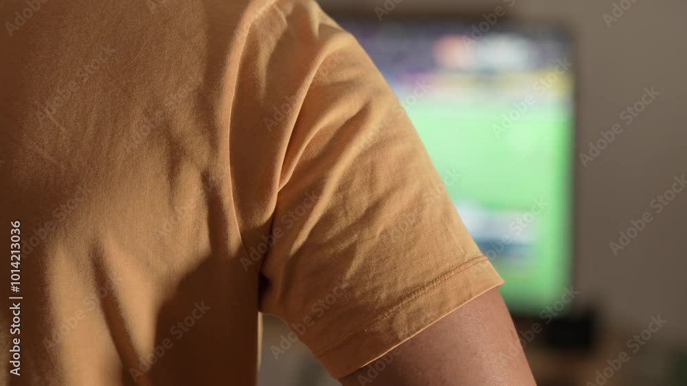 Soccer Fan in Yellow Jersey Watching a Game at Home While Pointing at the TV Soccer Fan in Yellow Jersey Watching a Game at Home While Pointing at the TV