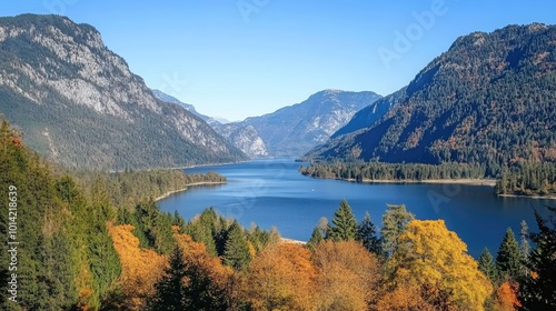 A stunning view of a mountain lake with lush autumn trees in the foreground and snow-capped mountains in the distance.