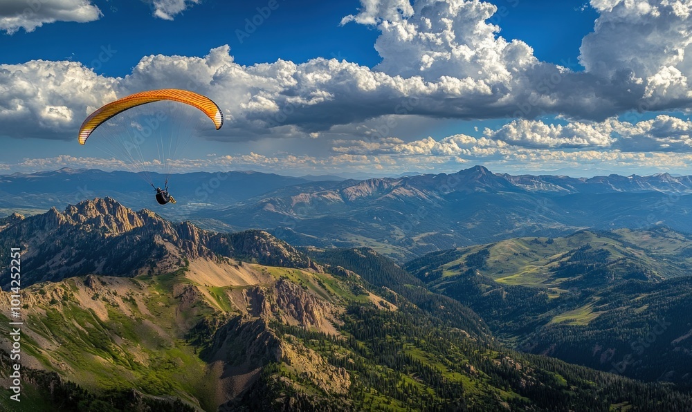 A paraglider soars through the sky above a mountain range with a clear blue sky and fluffy white clouds. A paraglider soars through the sky above a mountain range with a clear blue sky and fluffy white clouds.