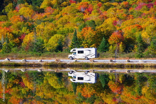 Fototapeta Naklejka Na Ścianę i Meble -  RV traveling on a NH road during fall foliage with reflection in lake