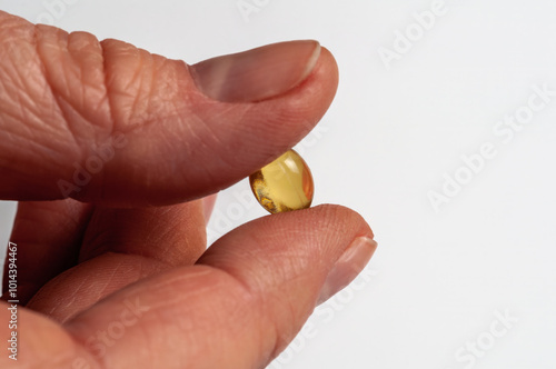 A close-up of a hand holding an Omega-3 fish oil capsule against a white background.