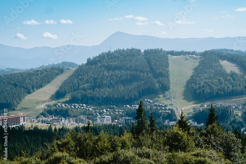 Scenic mountain view capturing ski slopes, lush forests, and a tranquil town nestled below in a summer landscape photo