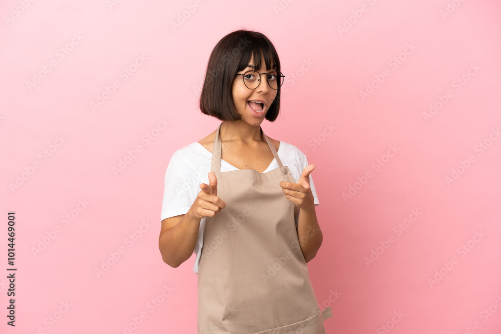 Restaurant waiter over isolated pink background surprised and pointing front Restaurant waiter over isolated pink background surprised and pointing front
