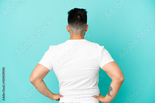 Young caucasian man isolated on blue background in back position