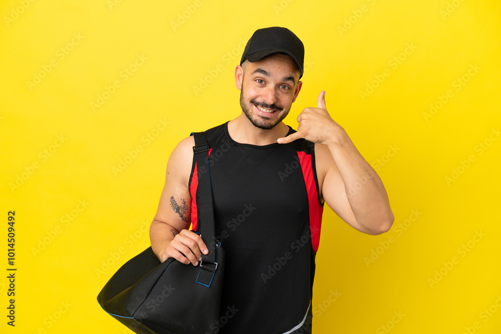 Young sport caucasian man with sport bag isolated on yellow background making phone gesture. Call me back sign Young sport caucasian man with sport bag isolated on yellow background making phone gesture. Call me back sign