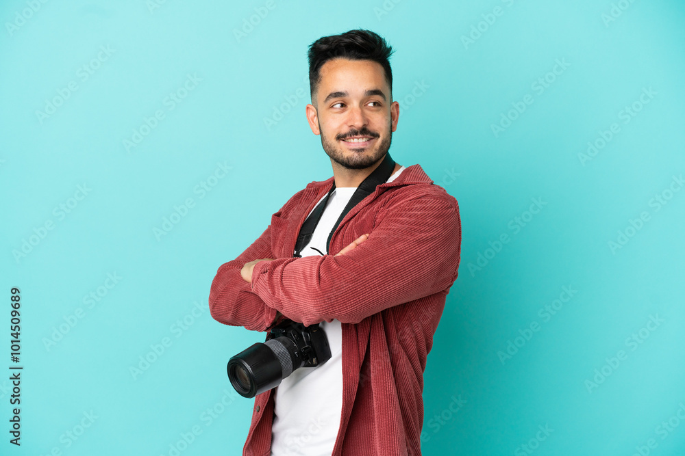 Young photographer caucasian man isolated on blue background with arms crossed and happy Young photographer caucasian man isolated on blue background with arms crossed and happy