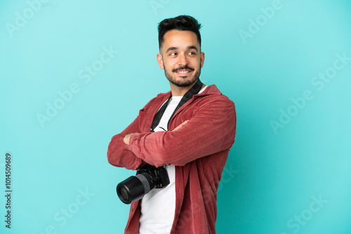 Young photographer caucasian man isolated on blue background with arms crossed and happy