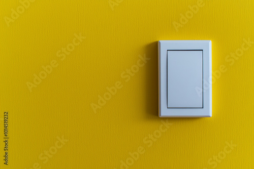 A simple white light switch mounted on a vibrant yellow wall, designed for controlling lighting in a room.