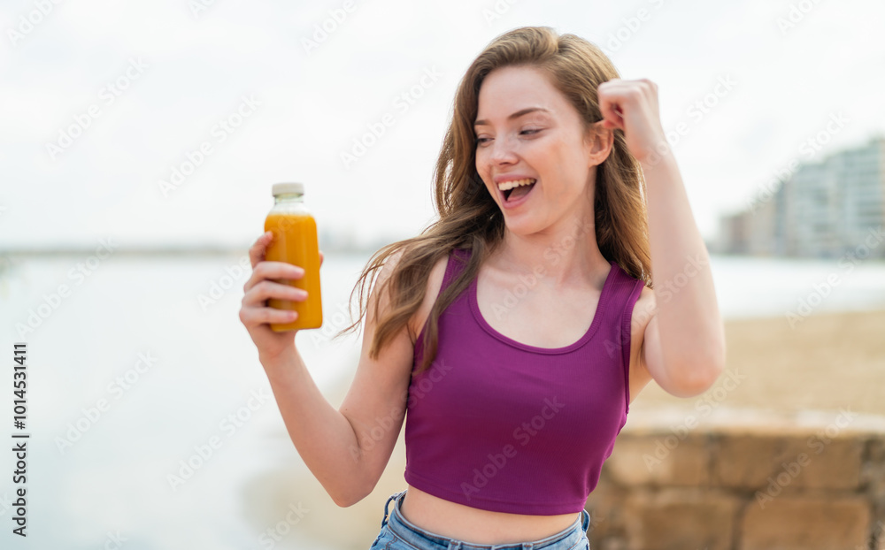 Young redhead girl holding an orange juice at outdoors celebrating a victory Young redhead girl holding an orange juice at outdoors celebrating a victory