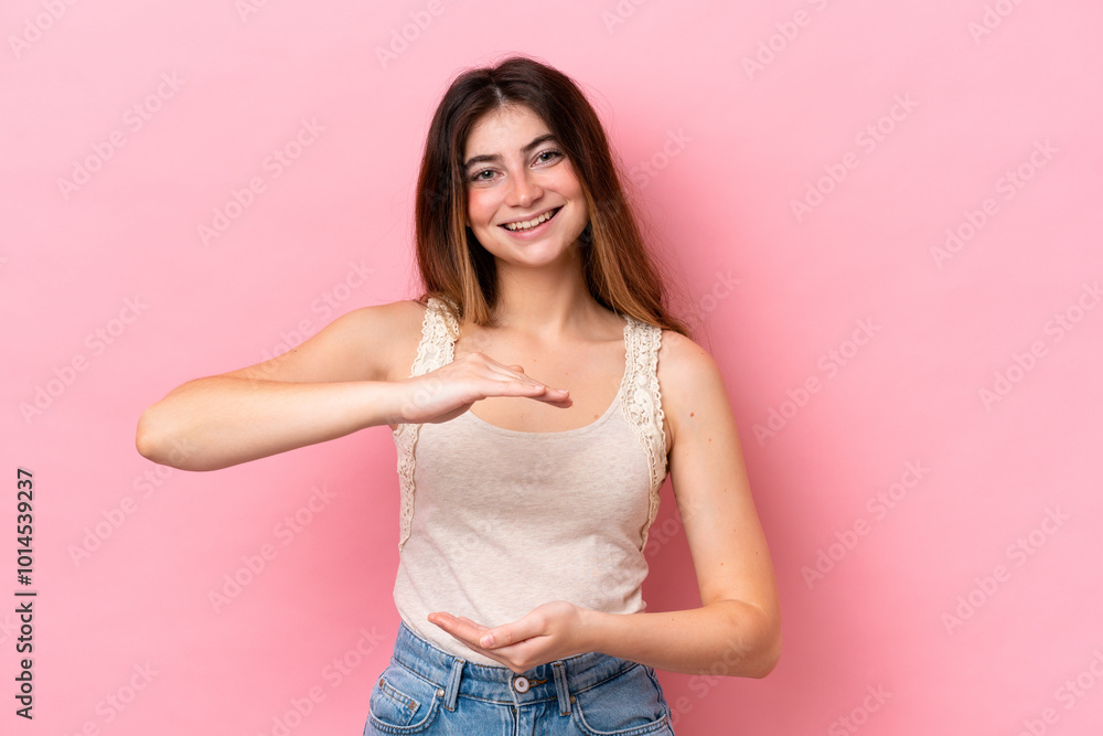 Young caucasian woman isolated on pink background holding copyspace imaginary on the palm to insert an ad Young caucasian woman isolated on pink background holding copyspace imaginary on the palm to insert an ad