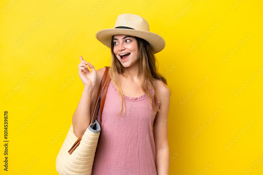 Young caucasian woman holding a beach bag isolated on yellow background intending to realizes the solution while lifting a finger up Young caucasian woman holding a beach bag isolated on yellow background intending to realizes the solution while lifting a finger up