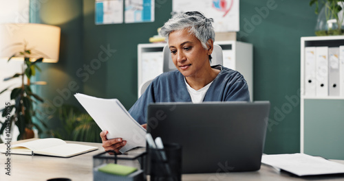 Doctor, laptop and mature woman with paperwork in office for healthcare, research or patient records. Medical professional, reading and work with info by tech for diagnosis review, report or feedback photo