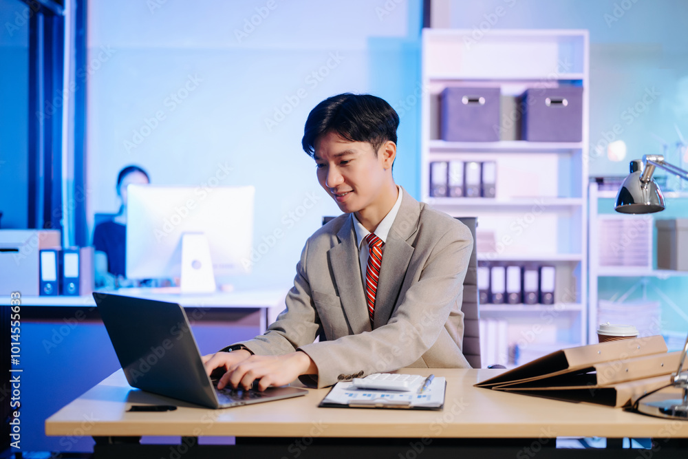 Asian Businessman analyzing reports in a modern office, working on a computer. Perfect for corporate, business, and over time concepts Asian Businessman analyzing reports in a modern office, working on a computer. Perfect for corporate, business, and over time concepts