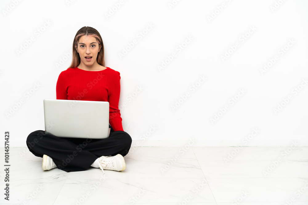 Φωτογραφία Young caucasian woman with a laptop sitting on the floor with surprise facial ex