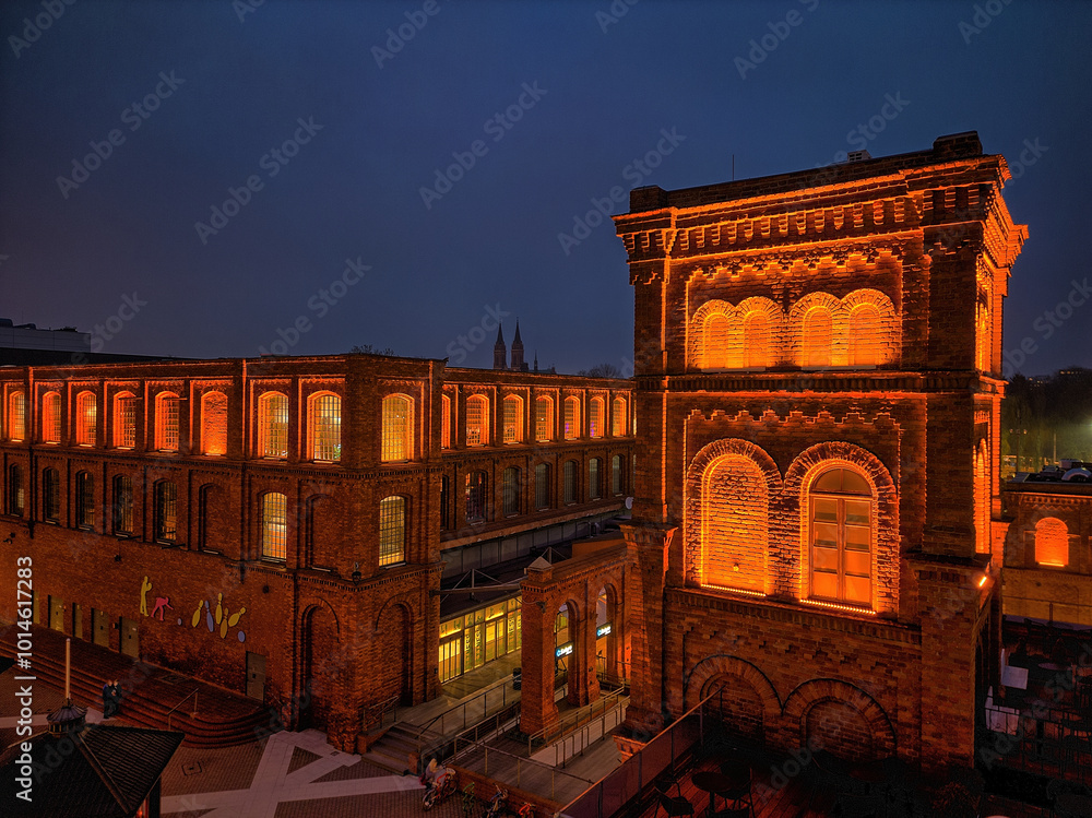 Nighttime View of Manufaktura in Łódź, Poland, Illuminated by Warm Lighting Against the Historic Red Brick Buildings and Open Public Square