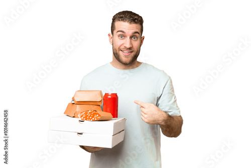 Young handsome blonde man holding pizzas and burgers over isolated background with surprise facial expression