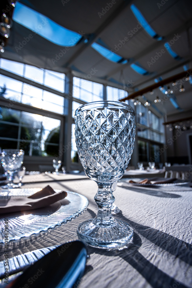 Crystal glass on the table in a bright, glass-walled banquet hall. Photo taken during the day, with sunlight streaming in.