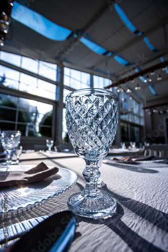 Obraz na płótnie Crystal glass on the table in a bright, glass-walled banquet hall. Photo taken during the day, with sunlight streaming in. w salonie
