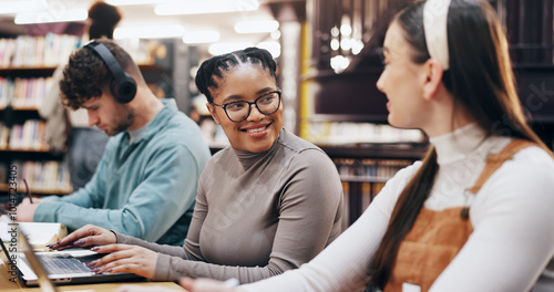 Students, happy and laptop in library for learning, brainstorming and research assignment. Women, smile and tech in university for social media post, comedy literature and pleased with test results