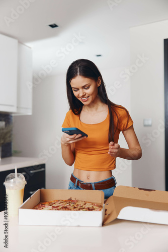 Woman checking her phone in front of a pizza box in a casual setting photo