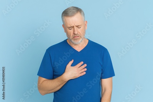 Man in blue t-shirt having chest pain, isolated on blue background, focus on his hand touching the area around his heart.