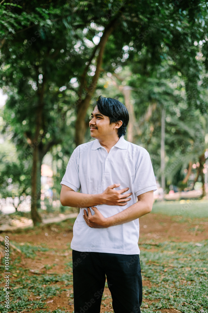 Southeast Asian man holding his stomach and chest, conveying discomfort or pain Southeast Asian man holding his stomach and chest, conveying discomfort or pain