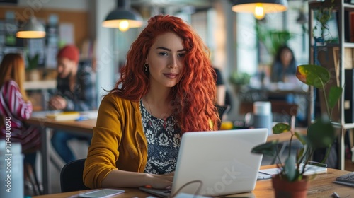 Middle eastern woman manager with red hair sitting at desk, using laptop in creative office, marketing agency