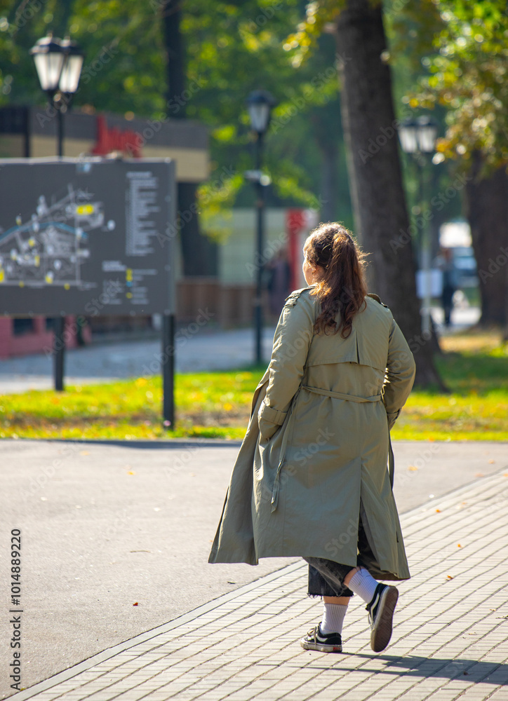 A woman wearing a green coat walks down a sidewalk A woman wearing a green coat walks down a sidewalk